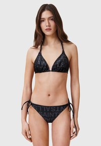 Set di bikini neri con top triangolare e spalline regolabili, slip a vita bassa, entrambi con un motivo logo ripetuto. Texture liscia.