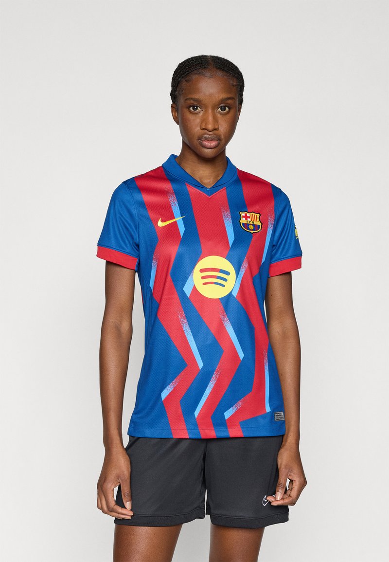 Φανέλα της FC Barcelona σε μπλε και κόκκινο με ζιγκζαγκ μοτίβο, λογότυπο της Nike και γραφικό κύκλο της Spotify. Μανίκια κοντά και σχέδιο με λαιμόκοψη V.