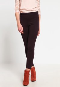 Vysoké hnědé legíny s hladkou texturou, doplněné světle růžovým topem a oranžovými kotníkovými botami.