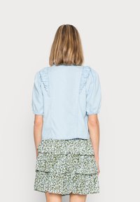 Jaqueta de denim azul clara com detalhes em renda nos ombros, combinada com uma saia rodada em camadas com padrão floral verde.