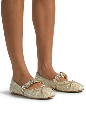 Ballerines dorées et beiges avec un tissu texturé, une bride ornée de strass transparents et un petit nœud sur le bout.