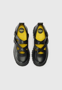 Black synthetic shoes featuring a rounded toe, crisscross straps, and a vibrant yellow insole. Equipped with a textured rubber sole for grip.