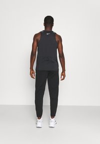Zwarte mouwloze sportshirt met een ronde hals en een achterzak, gecombineerd met strakke zwarte broek en witte sneakers.