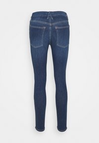 Jeans de denim azul oscuro y ajustados con cintura de media altura, cordón elástico y dos bolsillos traseros tipo parche. Terminados con un dobladillo limpio.