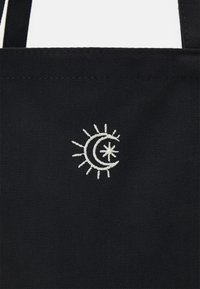 Sac fourre-tout en tissu noir avec un motif blanc brodé d'un croissant de lune partiellement recouvert par un soleil avec des rayons.
