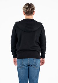 Felpa nera con cappuccio e finitura testurizzata, con polsini aderenti e fascia in vita, abbinata a jeans in denim blu con tasche posteriori.