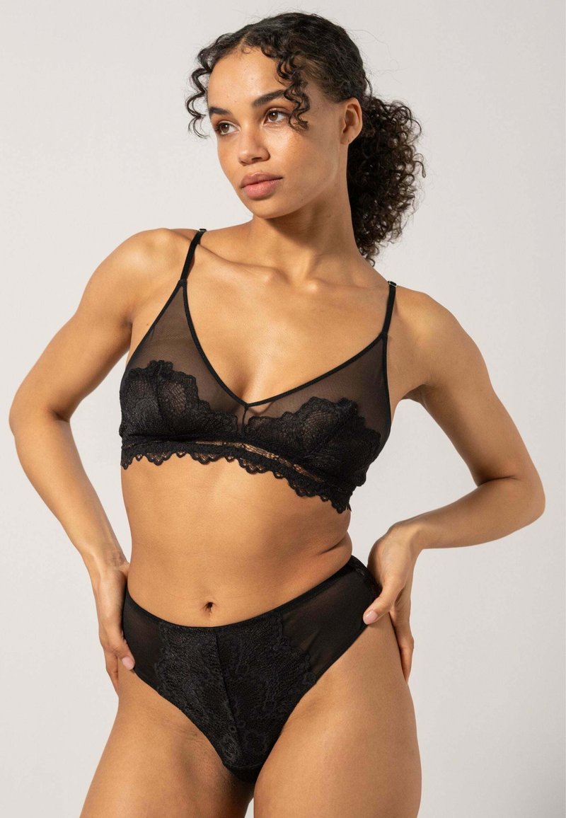 Svart underklänning set som innehåller en genomskinlig bralette med spetsdetaljer och matchande högmidjade trosor, som visar upp intrikata blommönster.
