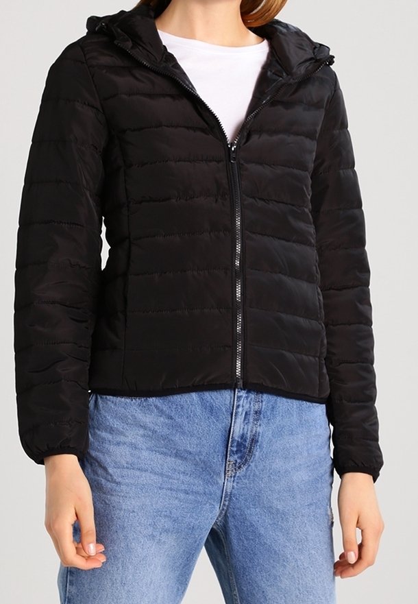 Schwarze Steppjacke mit Kapuze, Reißverschluss auf der Vorderseite, gestepptem Muster und elastischen Bündchen, kombiniert mit hellblauen Jeans.