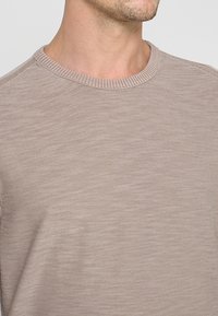 Beige trui met ronde hals en geribbelde boord. Gemaakt van gestructureerd gebreid materiaal, met een subtiel patroon en nette stiksels.