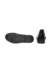 Scarpa di pelle nera con punta rotonda, tacco basso e suola in gomma strutturata con motivi circolari e dettaglio del logo.