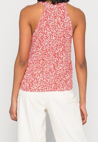 Červený a bílý halter top s vzorem a detaily v oblasti zad ve tvaru klíčové dírky, vyrobený z lehkého materiálu, fitted design, spárovaný s bílými kalhotami.