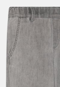 Calças de ganga cinzentas com uma textura suave, apresentando um bolso frontal e um laço para cinto. A costura é discreta e combina com a cor do tecido.