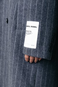 Palton gri din lână cu dungi verticale albe, având o etichetă pe mânecă, patru nasturi și o textură moale.