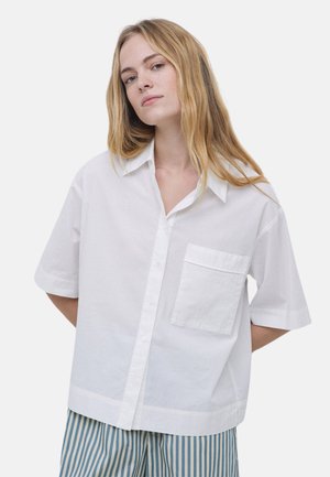 Camisa blanca de manga corta abotonada con collar puntiagudo, bolsillo en el pecho y corte relajado. Tela de algodón texturizada, superficie suave.