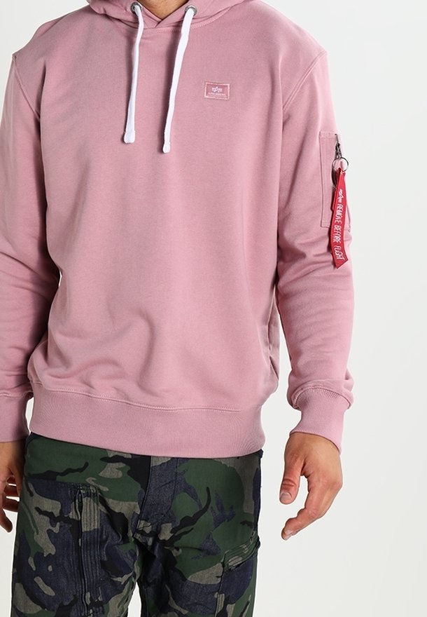 Felpa rosa chiaro in tessuto morbido, con lacci bianchi, una piccola patch con logo e una tasca con zip rossa sulla manica.