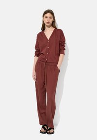 Zestaw odzieży loungewear w kolorze terakoty, składający się z kardiganu z dekoltem w kształcie V oraz spodni na sznurku, wykonany z miękkiego materiału o luźnym kroju.