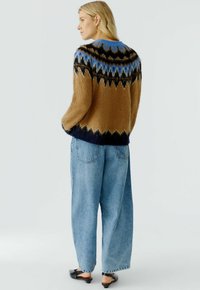 Bruine en blauwe gebreide trui met een fuzzy textuur, voorzien van een ronde hals en een contrasterende marineblauwe onderkant. Gecombineerd met lichtblauwe losse jeans.