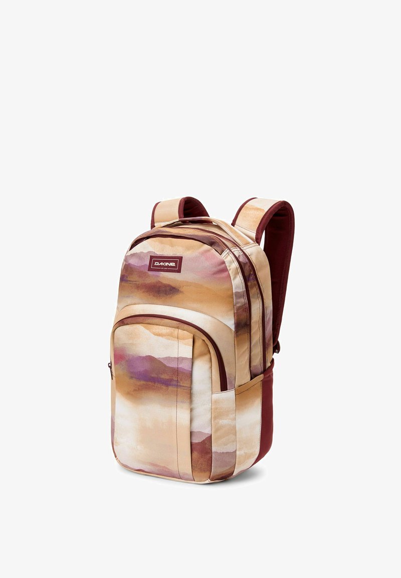 Zaino Dakine con spallacci imbottiti in tonalità di beige, rosa e marrone, caratterizzato da un design di montagne in acquerello e una tasca frontale con zip.