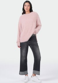 Lichtroze, fluffige gebreide trui met een ronde hals en verlaagde schouders, gecombineerd met donkergrijze wijde jeans en witte sneakers.