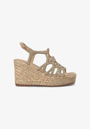 Sandalia cuña en beige claro con suela de yute trenzado. Presenta puntera abierta, diseño con recortes y piedras brillantes decorativas en las correas.