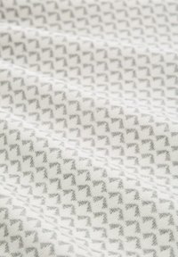 Tissu textile blanc avec un motif géométrique texturé en gris, présentant de petites formes angulaires et une finition douce et tissée.