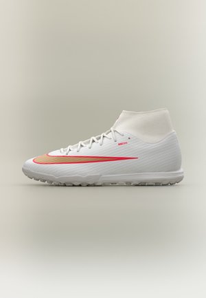 Hvid mid-top fodboldsko med rød og gylden Nike swoosh og tekstureret sål på en neutral baggrund.