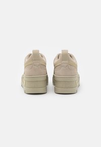 Un paio di sneakers Puma in suede beige viste da dietro, con linguette e suole a piattaforma testurizzate su uno sfondo bianco.