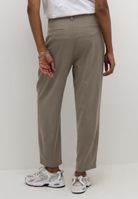 Beige op maat gemaakte broek met een rechte snit, voorzien van twee achterzakken en zijsplitten aan de zoom, gecombineerd met grijze sportschoenen.
