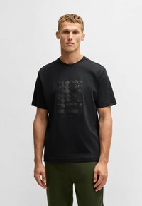 Sort kortærmet t-shirt lavet af glat stof, med et tonalt geometrisk mønster foran og rund halsudskæring. Ensfarvet ryg.