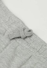 Světlá šedá tkanina s texturovaným povrchem, s poutkem na tkaninu a vodorovným prošíváním podél pasu.