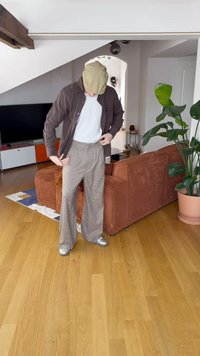 Brown button-up shirt, white t-shirt, and plaid wide-leg trousers. Silver shoes. Background features a couch and potted plant.