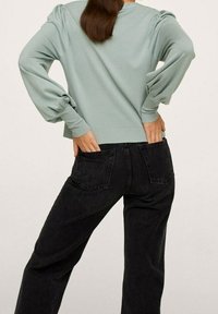 Jasnozielony pulower z bufkami na rękawach, ściągaczami na mankietach i dole, zestawiony z czarnymi, wysokim stanem, jeansami z tylnymi kieszeniami.