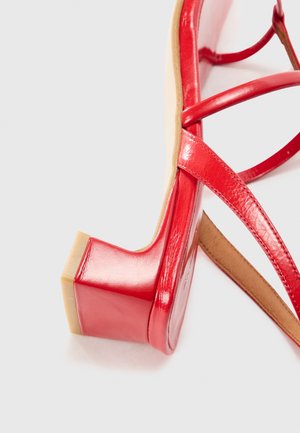 Rød patentlæder sandal med en tyk blokhæl, krydsende stropper og en glat overflade. Udsat indre foring i beige.