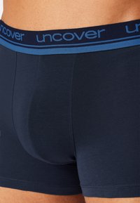 Dark navy boxer briefs made from a smooth fabric, featuring a contrasting blue waistband with the brand name "uncover" in clear lettering.