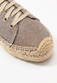 Sneaker espadrille tissé marron avec un upper en tissu métallique texturé, lacets beiges et une semelle enveloppée de jute. Œillets dorés et accents de coutures.