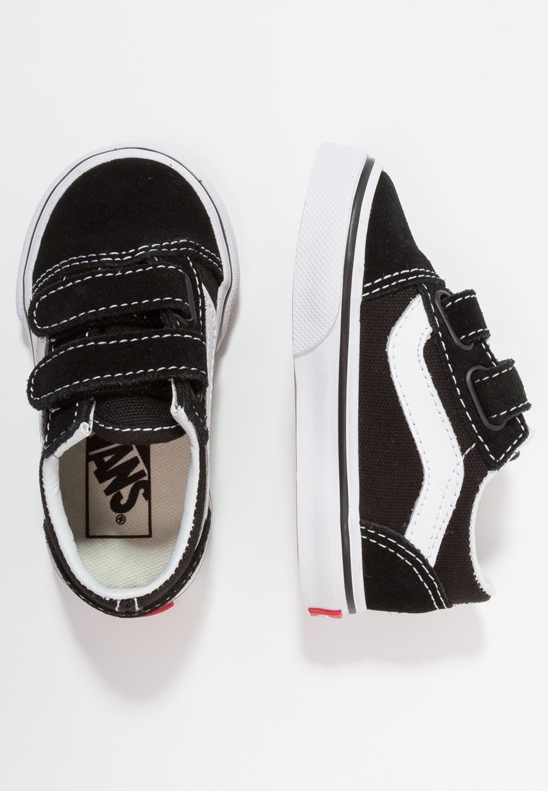 Baskets noir et blanc pour tout-petit avec deux brides velcro, semelles blanches et logo Vans à l’intérieur de la chaussure.