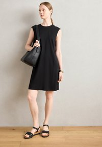Black sleeveless dress with a relaxed fit, paired with black leather handbag and black sandals featuring straps and a wooden platform.