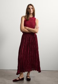 Completo due pezzi bordeaux composto da una parte superiore senza maniche testurizzata e una gonna maxi plissettata, abbinato a scarpe flat coordiante.