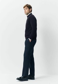 Navy sweater with a high collar, paired with dark patterned trousers and black shoes. The outfit has a slim fit and smooth texture.