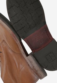 Chaussures de ville en cuir marron avec une tige lisse et une semelle en caoutchouc noir présentant un motif texturé et un détail de talon en bois.