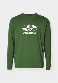 Langermet grønn bomull t-skjorte med et hvitt ovalt logo med en diamantform og "VOLCOM" -teksten sentrert under.