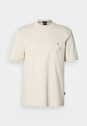 T-shirt de manga curta e gola redonda em algodão bege claro. Apresenta um pequeno logótipo redondo no peito e uma bainha reta.