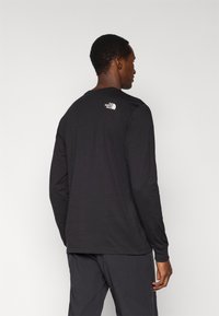 Μαύρο μακρυμάνικο μπλουζάκι από βαμβακερό μείγμα, με μικρό λευκό λογότυπο στο επάνω μέρος της πλάτης, με στρογγυλή λαιμόκοψη και κανονική εφαρμογή.