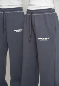 Sivé tepláky s elastickým pásom a šnúrkou. Na prednej strane sa nachádza biele logo "MULTIPLY APPAREL" a ich textura je hladká.