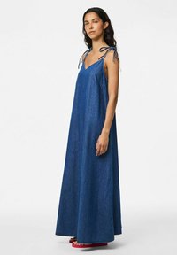 Denim maksi haljina u tamnoplavoj boji sa tankim naramenicama i V-izrezom. Ima slobodan kroj i bočne džepove radi dodatne praktičnosti.