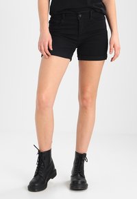 Černé denimové šortky s ohrnutými manžetami, s knoflíkovým a zipovým zapínáním. Kombinované s černými šněrovacími botami, na šedém pozadí.