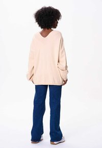 Crèmekleurige gebreide trui met een V-hals en een oversized pasvorm, gecombineerd met blauwe flare jeans en witte sneakers.