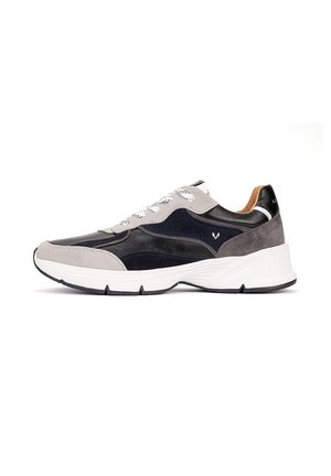 Zapatilla deportiva negra y gris para hombre con suela blanca y cordones, diseño bajo y paneles texturizados de ante y cuero.