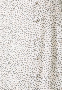 Tissu à motifs avec une base blanche et des taches grises éparpillées ; comporte cinq boutons le long du côté gauche ; surface douce et texturée.