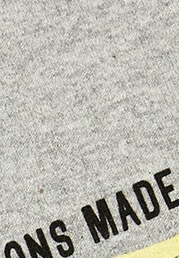 Harmaa kangas, jossa on tekstuuri ja mustalla printatulla tekstillä, joka lukee "MADE" ja "ONS." Kankaan alaosassa näkyy keltainen reunus.